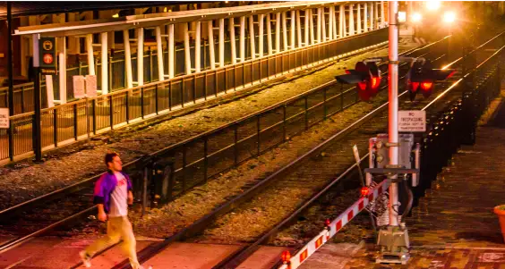 SunRail Get A Clue Photo 2 - Man running across tracks with crossing arms down and train approaching.